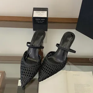 Close-up of black pointed-toe woven hollow-out high heel mule sandals on a glass table