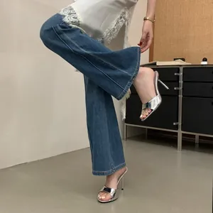 Close-up of metallic silver high-heeled mule sandals worn with flared denim jeans