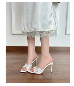 Elegant white lace pointed toe high heel mules on model standing on wooden floor.