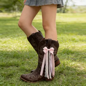 Close-up detail of a pink bow with pearl and lace ribbon charms on brown cowboy boots