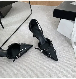 Vista detallada de tacones negros de punta con hebillas y tachuelas estilo punk.