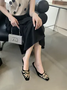Primer plano de elegantes mules de terciopelo negro con bordado floral dorado