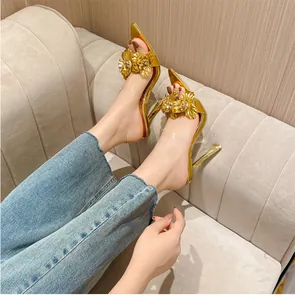 Gros plan de sandales à talons hauts dorées avec fleurs 3D et bride transparente