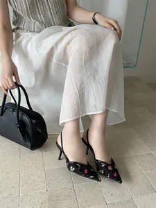 Primer plano de zapatos destalonados de malla negra con delicado bordado floral rosa