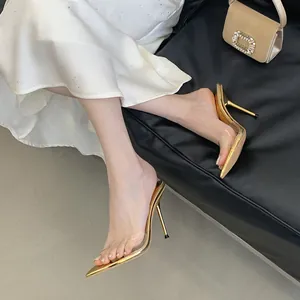 Close-up detail of elegant gold stiletto mules with clear transparent straps on a model.