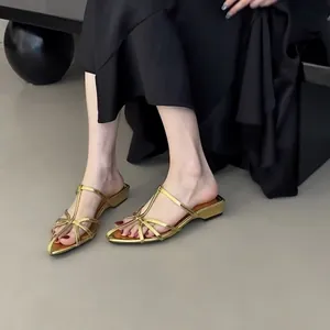 Gros plan d'élégantes mules dorées à lanières, bout pointu et petit talon avec robe noire