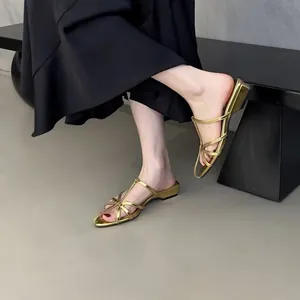 Vue détaillée de sandales dorées à lanières et petit talon portées avec une robe noire.