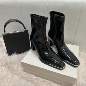Macro view of black patent leather ankle boots with square toe and silver metal trim