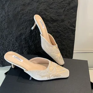 Vista detallada de mules beige con tacón de aguja, bordado floral dorado y punta cuadrada