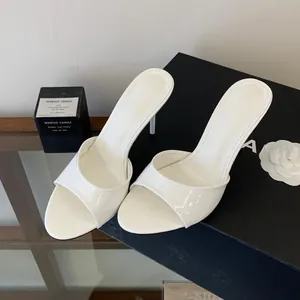 Detail view of white patent leather open-toe stiletto heel mules on a black background