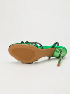 Detailed view of emerald green rhinestone stiletto sandal with metallic finish heel