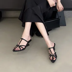 Gros plan d'élégantes mules noires à lanières et bout pointu avec petit talon au pied