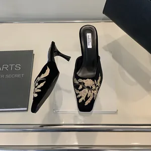 Primer plano de mule de terciopelo negro con bordado floral dorado y puntera cuadrada.
