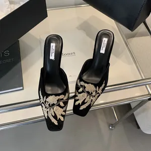 Primer plano de mules negros con bordados florales crema y elegante diseño de punta cuadrada