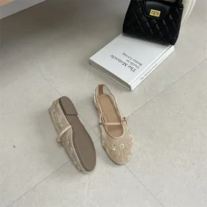 Detail view of beige mesh flats with floral embroidery and thin strap on a grey floor.