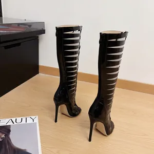 Detailed rear view of sexy black patent leather cut-out stiletto tall boots on wood floor