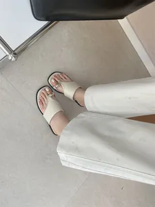 Stijlvolle beige platte teensandalen met gouden gesp gedragen met witte broek detail.
