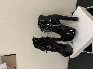 Close-up of black patent leather platform boots with metal chains and rivets.