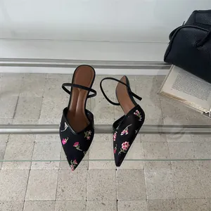 Vista detallada de tacones destalonados de malla negra con bordado floral rosa delicado