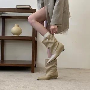 Close-up side view of elegant beige pointed-toe slouchy wedge boots worn by a model