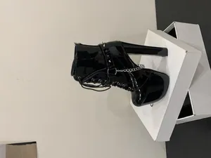 Side view detail of black patent leather platform boots with metal chains and rivets