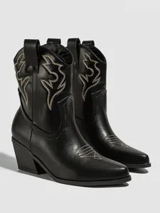Detailed view of black cowboy boots with intricate beige embroidery and a block heel.