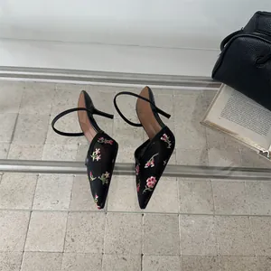 Vista detallada de elegantes mules de malla negra con bordado floral y tacones de aguja en estilo retro