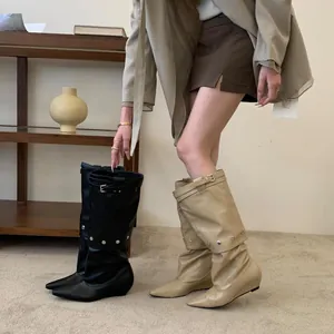 Detail of slouchy knee-high boots with pointed toe and metal buckle accents.