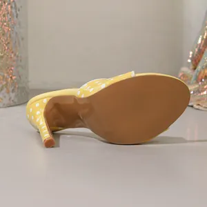 Detailed close-up showing the brown sole and stiletto heel of a yellow polka-dot mule