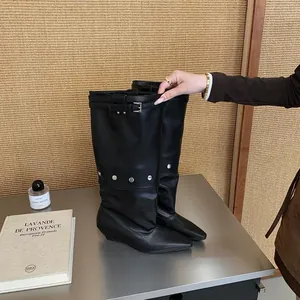 Close-up detail of black leather pant-tube boots featuring buckle strap and silver studs