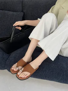 Detailopname van bruine platte teenslippers met zilveren metalen gesp op een model