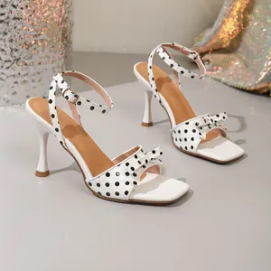 Detailweergave van witte polkadotsandalen met elegante strik en vierkante neus.