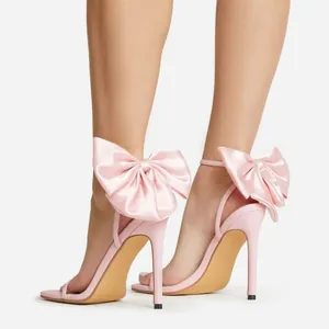 Primo piano di eleganti sandali rosa con tacco a spillo, fiocchi in raso e punta quadrata