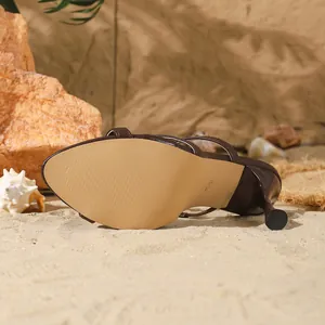 Vue détaillée de mules stiletto marron sur sable montrant la semelle et le talon