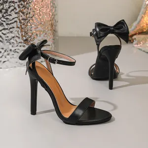 Close-up of black stiletto sandals featuring a large bow and ankle strap