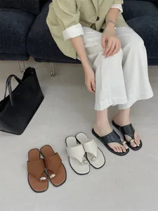 Detailopname van minimalistische platte teensandalen met een metalen gesp detail