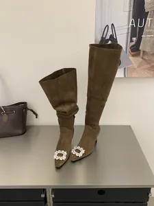 Close-up detail of brown suede pointed toe boots featuring sparkling rhinestone buckle