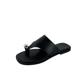 Detailopname van minimalistische zwarte teenslippers met een zilveren kraal-accent