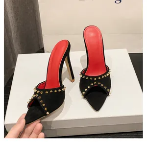 Detailweergave van zwarte suède muiltjes met hoge hakken met gouden studs en rode zolen