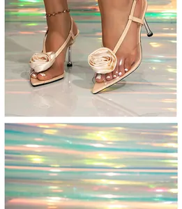 Dettaglio ravvicinato dell'elegante decorazione floreale beige su sandali a spillo trasparenti.