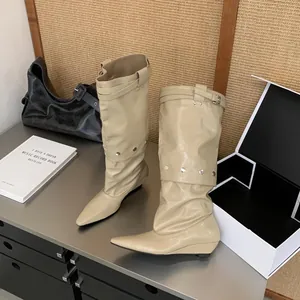 Detailed full view of beige pointed-toe wedge high boots with buckle and studs