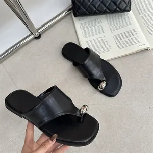 Detail van zwarte slippers met teensluiting en zilveren metalen accent op platte zool