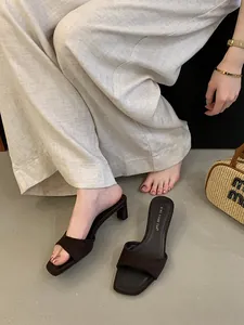 Dettaglio di sabot marroni a punta quadrata con tacco largo e pantaloni di lino