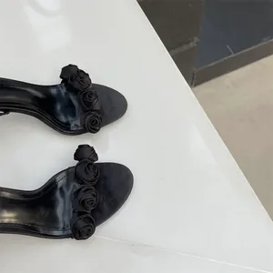 Nahaufnahme eleganter schwarzer Sandaletten mit dekorativen Satinrosen am Riemen.