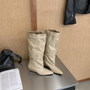 Stylish beige pointed-toe slouchy boots with buckles and metal studs on a table.
