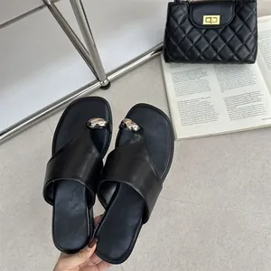 Detailopname van zwarte platte leren sandalen met een metallic zilveren teenringversiering.