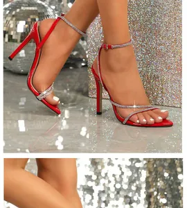 Primo piano di sandali rossi con tacco alto e cinturini incrociati in strass su una modella.