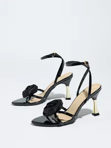 Elegant black satin high heel sandals featuring a delicate rose flower and gold stiletto.