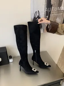Close-up of black stiletto over-the-knee boots with rhinestone square buckle and pointed toe.
