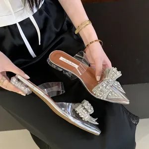 Nahaufnahme eleganter Pantoletten mit durchsichtigem Blockabsatz, Strassschleife und PVC.